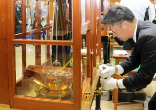 鍋のような分銅に入れた硬貨の重さをてんびんで慎重に計る職員＝大阪市北区天満１