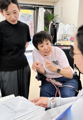 介助者の援助を受けて働く田中順子さん（中央）＝神戸市東灘区