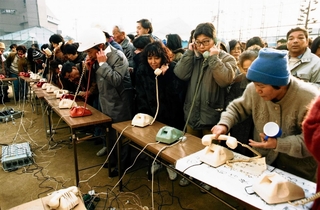激震地では家族や知人との連絡手段がなくなり、仮設電話は安否を伝える人たちでごった返した＝１９９５年１月１８日、神戸市長田区、蓮池小学校
