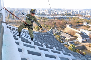 大天守の屋根に乗り、ほうきで汚れを落とす自衛隊員＝16日午前、姫路市本町