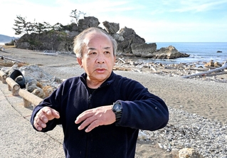 希望の灯りへの思いを語る刀祢聡さん。奥に見える窓岩は地震で上部が崩落した＝１２月２３日、石川県輪島市町野町曽々木（撮影・斎藤雅志）