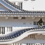 大天守の屋根に乗り、ほうきで汚れを落とす自衛隊員＝16日午前、姫路市本町