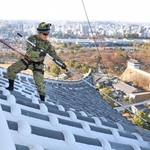 大天守の屋根に乗り、ほうきで汚れを落とす自衛隊員＝16日午前、姫路市本町