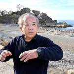 希望の灯りへの思いを語る刀祢聡さん。奥に見える窓岩は地震で上部が崩落した＝１２月２３日、石川県輪島市町野町曽々木（撮影・斎藤雅志）