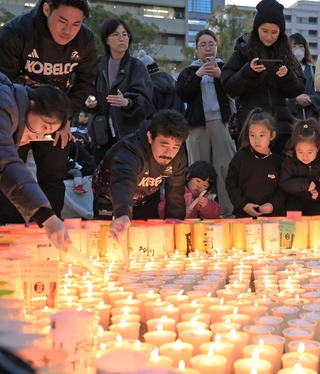 「つむぐ」の文字に並べた紙灯籠に火をともすコベルコ神戸スティーラーズの日和佐篤（手前中央）ら＝神戸市中央区加納町６（撮影・丸山桃奈）