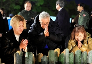 手を合わせる向邦男さん（中央）と妻千鶴さん（右）、孫の池田睦さん＝１７日午前６時１９分、神戸市中央区加納町６、東遊園地（撮影・中西幸大）