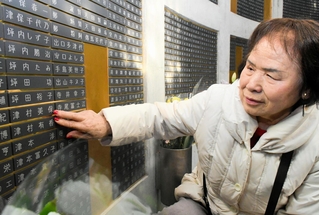 震災で犠牲になった長女津村美保さんと孫の有香ちゃんの名前が記された銘板に触れる森本律子さん＝１月１７日午前１０時４分、神戸市中央区加納町６、東遊園地