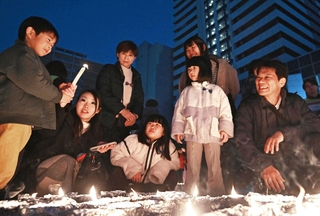 犠牲者を追悼する催しで、子どもが手にしたろうそくの火を見つめる人たち＝１７日午後５時４１分、神戸市長田区若松町４、ＪＲ新長田駅前（撮影・風斗雅博）