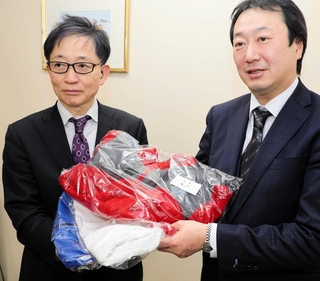 神戸マラソン実行委員会事務局の脇本禎久総務部長（左）に衣類を手渡す白星社クリーニングの石井大社長＝神戸市灘区琵琶町３