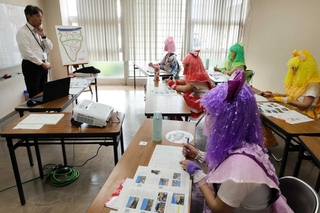 「シン・温泉検定」で新温泉町のアイドル「ももいろクロおばあＺ」に講義する町おんせん天国室の谷口薫室長（左）＝２０２４年１０月、同町浜坂