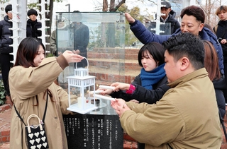 「１．１７希望の灯り」の火を輪島市へ。届けるランタンに火を移す参加者たち＝１月31日午後、神戸市中央区加納町６、東遊園地