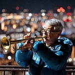 神戸の街を背に、トランペットの音色を響かせる松平晃さん＝２０２５年１月１７日、神戸市中央区、ビーナスブリッジ