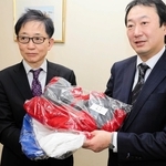 神戸マラソン実行委員会事務局の脇本禎久総務部長（左）に衣類を手渡す白星社クリーニングの石井大社長＝神戸市灘区琵琶町３