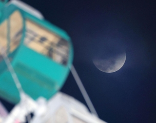 部分食の後半に差しかかった月。左は淡路サービスエリアの大観覧車＝３日午後９時４２分、淡路市岩屋から（撮影・吉田敦史）