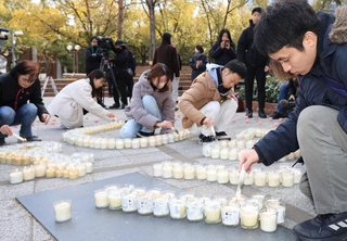 東日本大震災の被災地に思いをはせ、キャンドルに火を付ける人たち＝１１日午後、神戸市中央区加納町６、東遊園地（撮影・吉田敦史）