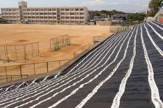 グラウンド脇ののり面に敷かれた防草シート「イジゲンシート」＝神戸市西区伊川谷町長坂、長坂中学校