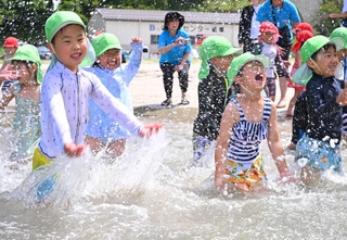 波打ち際で水をかけ合う園児たち＝25日午前、諸寄・塩谷浜海水浴場