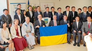 ウクライナ国旗を持つ（右から）黒川治県議、ユーリ・ルトビィノフ駐日ウクライナ大使、岡部芳彦・神戸学院大教授ら＝神戸市中央区港島１（スビトラーナ・ローガンさん提供）