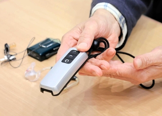 マイクの音声を電波で送り、受信機を内蔵した補聴器で聞く「ＦＭ補聴システム」を手に取る男性＝三田市内