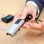 マイクの音声を電波で送り、受信機を内蔵した補聴器で聞く「ＦＭ補聴システム」を手に取る男性＝三田市内