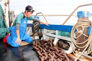 漁船に隠れたヌートリアを見つめる内海兼心さん＝淡路市育波