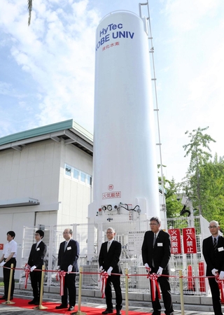 テープカットで液体水素貯槽（中央）の完成を祝う関係者。左奥の建物が水素実験棟＝神戸大学深江キャンパス