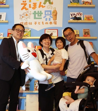 西栄一副館長（左端）から、３万人目の記念品を受け取る稲田京香さん（中央）と家族＝神戸市東灘区向洋町中２、神戸ファッション美術館