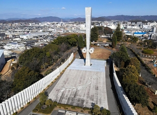 姫路の街並みを見守るように立つ「太平洋戦全国戦災都市空爆死没者慰霊塔」＝２０２５年１２月、姫路市西延末（ドローンで撮影）