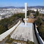 姫路の街並みを見守るように立つ「太平洋戦全国戦災都市空爆死没者慰霊塔」＝２０２５年１２月、姫路市西延末（ドローンで撮影）