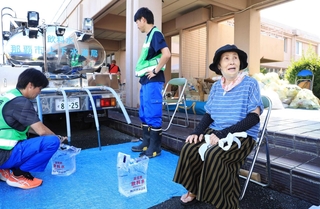 避難所で給水を受ける浜田えい子さん（右）＝熊本県八代市鏡町内田、鏡コミュニティセンター（撮影・吉田敦史）