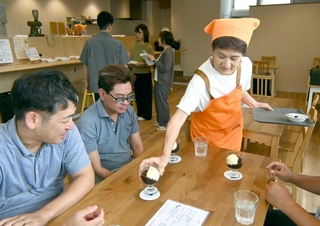 喫茶メニューを提供するかりばにあんの井上佐世さん。後ろは設備について説明を受ける見学者ら＝かりばキッチン