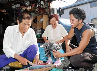 桑名金太郎さん（右端）のリクエストに応じ、手際よく魚をさばく満行さんと寿々代さん。ありのままの日常と魚談義が人気だ＝淡路市育波