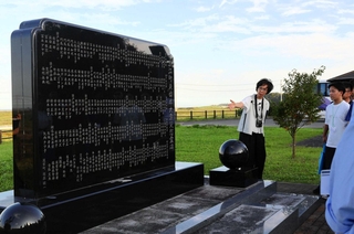 慰霊碑の前で、高校生らに東日本大震災時の状況を伝える大塚淳子さん（中央）＝福島県浪江町