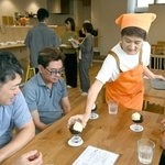 喫茶メニューを提供するかりばにあんの井上佐世さん。後ろは設備について説明を受ける見学者ら＝かりばキッチン