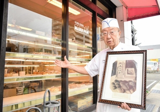 「献上のパン」の写真を手に店の歴史を語る須磨マル井パン店主の藤井英則さん＝神戸市須磨区須磨浦通４