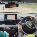 目隠しをした運転手（右）が助手席のコ・ドライバーの指示を聞いて運転する。バックミラーにアイマスクを着けた顔が映る＝神戸市西区岩岡町古郷