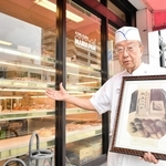 「献上のパン」の写真を手に店の歴史を語る須磨マル井パン店主の藤井英則さん＝神戸市須磨区須磨浦通４