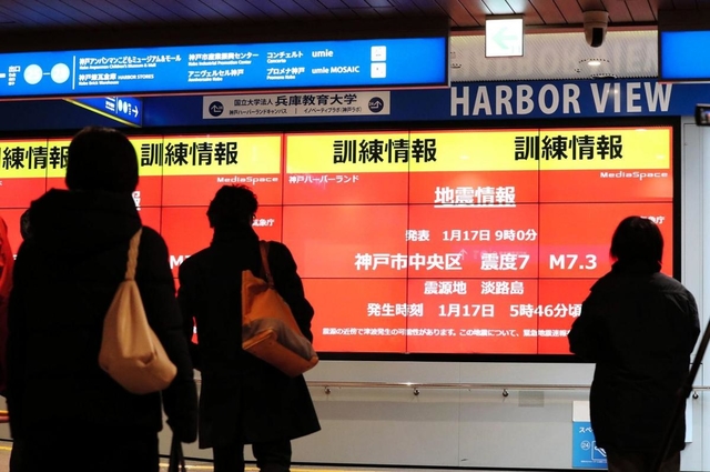 訓練用の地震情報が映し出されたデジタルサイネージ（電子看板）を見つめる人たち＝１７日午前９時６分、神戸市中央区東川崎町１（撮影・大山伸一郎）