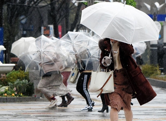 激しい風を受け、身をかがめて歩く人たち＝２７日午後３時１３分、神戸市中央区東川崎町（撮影・中西幸大）