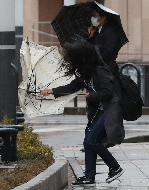 強風に傘を壊される女性＝２７日午後２時４４分、神戸市中央区東川崎町１（撮影・吉田敦史）