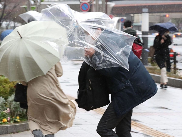 強風でひしゃげたビニール傘を差して歩く男性＝２７日午後２時３２分、神戸市中央区東川崎町１（撮影・吉田敦史）