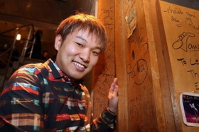 店内の柱に初めて書いた自身のサインとともに笑顔を見せる松永貴志さん＝２９日夜、芦屋市東山町（撮影・風斗雅博）