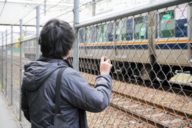 通過するＪＲの電車を見つめるＢさん。事故で背骨を骨折。後遺症で首から腰に痛みが残り、背中には湿布薬の跡が染み付いている＝伊丹市内