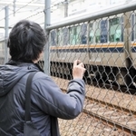 通過するＪＲの電車を見つめるＢさん。事故で背骨を骨折。後遺症で首から腰に痛みが残り、背中には湿布薬の跡が染み付いている＝伊丹市内