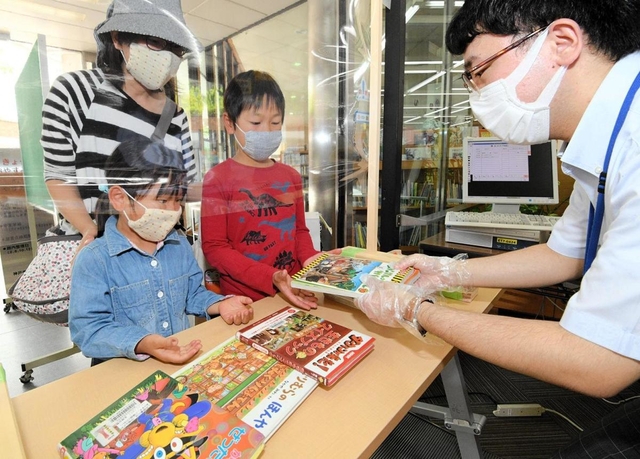 マスク姿で手袋をはめた図書館職員から予約していた本を受け取る子どもたち＝１７日午前、神戸市中央区楠町７、市立中央図書館（撮影・後藤亮平）