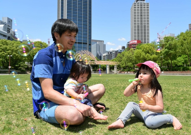 芝生の上でシャボン玉をして遊ぶ親子。日中に遊びに出たのは久しぶりといい、子どもたちも満足そうな笑顔だった＝２４日午後、神戸市中央区の東遊園地