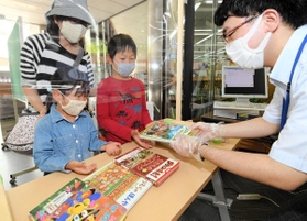 マスク姿で手袋をはめた図書館職員から予約していた本を受け取る子どもたち＝１７日午前、神戸市中央区楠町７、市立中央図書館（撮影・後藤亮平）