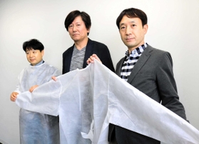 かばんの縫製技術を生かした医療用ガウンを手にする兵庫県鞄工業組合の由利昇三郎理事長（中央）ら＝豊岡市役所