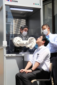 ウオークスルー方式で、ボックス内から検体を取る動作を見せる神戸市医師会の置塩隆会長（左奥）＝神戸市中央区