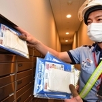 マンションの郵便受けにマスクを入れていく配達員＝１３日午後、神戸市中央区（撮影・秋山亮太）
